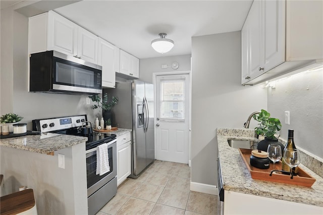 kitchen featuring light tile patterned floors, light stone counters, stainless steel appliances, a sink, and white cabinetry