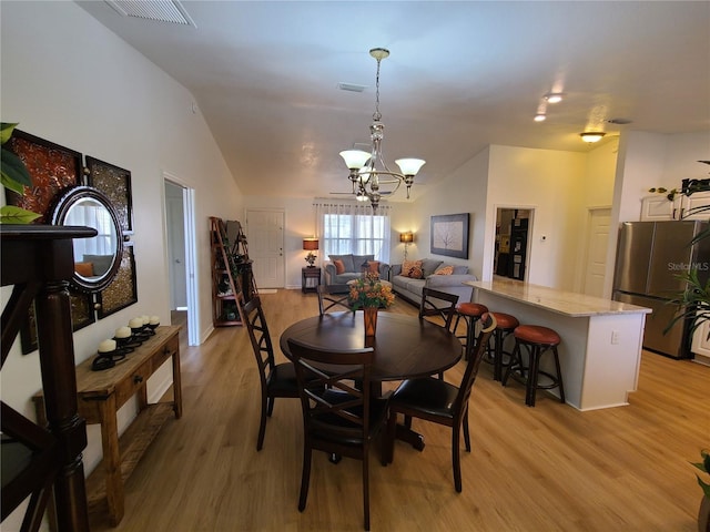 dining space with vaulted ceiling, light wood-type flooring, visible vents, and a notable chandelier