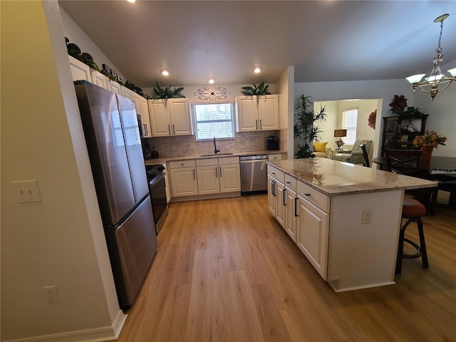 kitchen featuring decorative light fixtures, appliances with stainless steel finishes, white cabinets, a kitchen island, and a sink