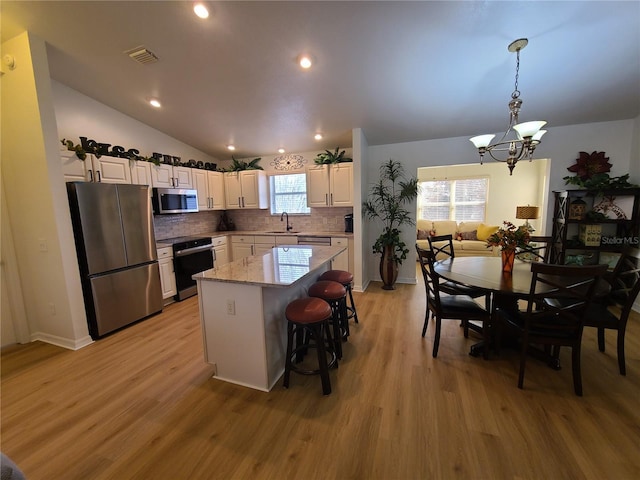 kitchen with visible vents, a center island, stainless steel appliances, white cabinetry, and a sink