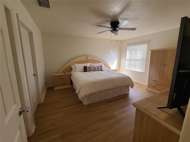 bedroom with baseboards, visible vents, a ceiling fan, wood finished floors, and a textured ceiling