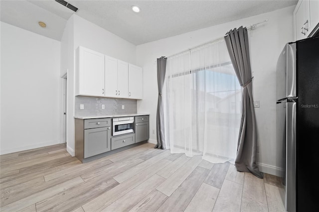 kitchen featuring light wood finished floors, gray cabinets, light countertops, appliances with stainless steel finishes, and white cabinets