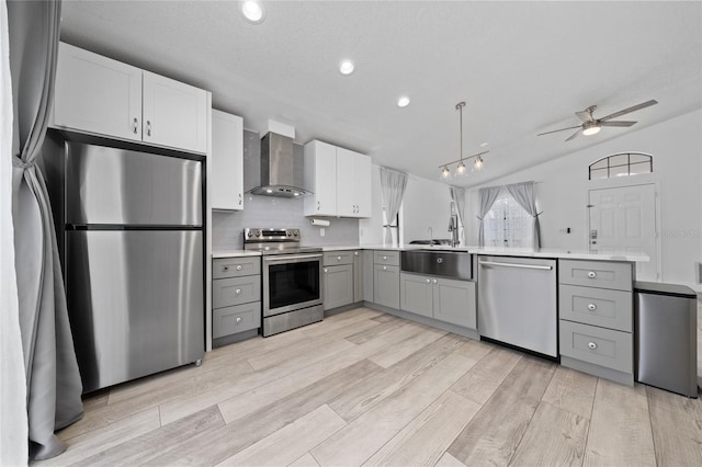 kitchen featuring appliances with stainless steel finishes, gray cabinets, light countertops, and wall chimney range hood