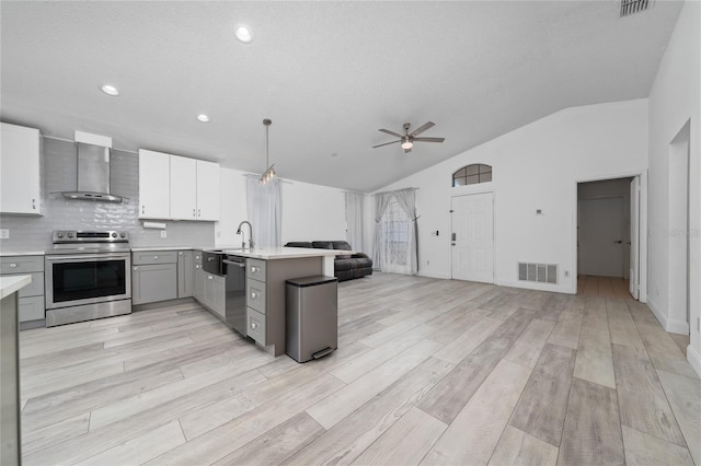 kitchen featuring open floor plan, decorative light fixtures, stainless steel appliances, light countertops, and wall chimney range hood