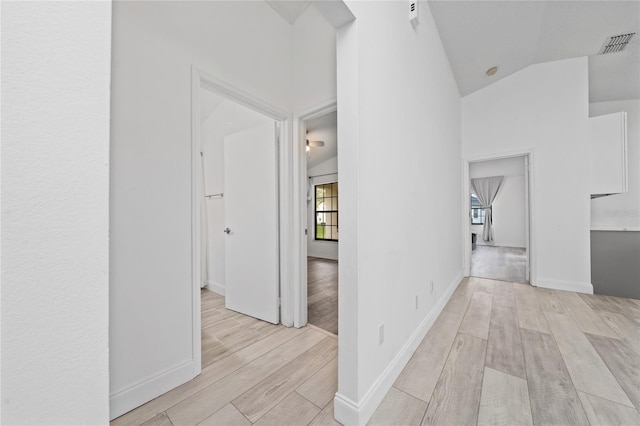 hall with light wood-type flooring, baseboards, visible vents, and vaulted ceiling