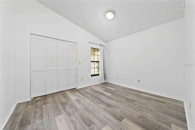 unfurnished bedroom with light wood-style flooring, baseboards, vaulted ceiling, and a closet