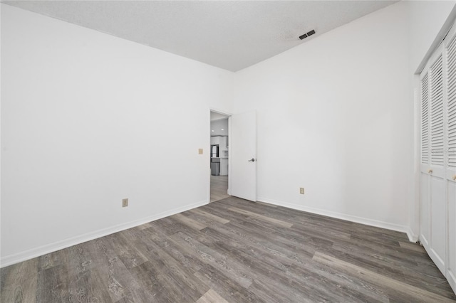 unfurnished bedroom with dark wood-style floors, baseboards, visible vents, and a closet