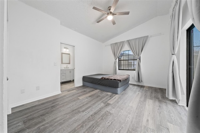 bedroom with a ceiling fan, baseboards, vaulted ceiling, light wood-style floors, and ensuite bath