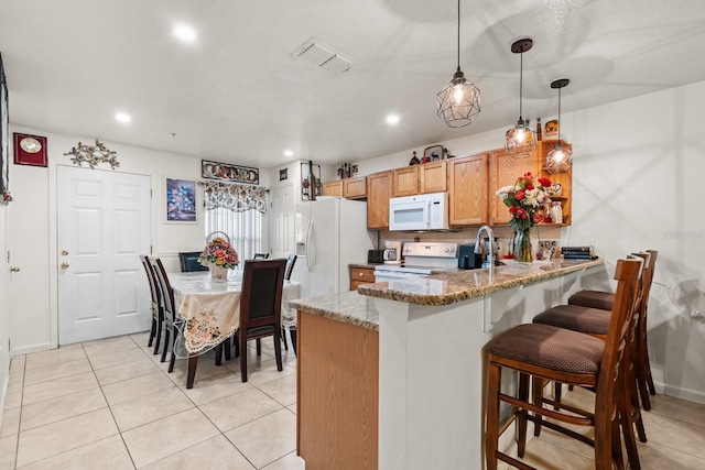 kitchen featuring light stone counters, a peninsula, white appliances, visible vents, and pendant lighting