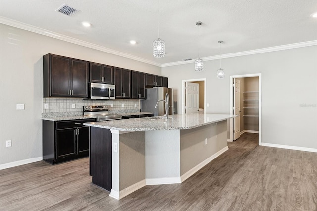 kitchen featuring stainless steel appliances, hanging light fixtures, backsplash, light wood-style flooring, and an island with sink