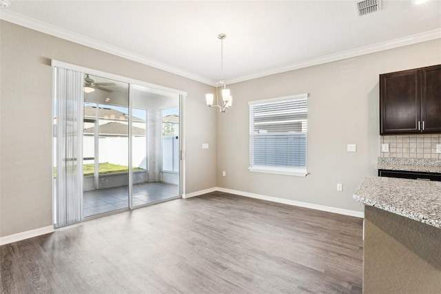 unfurnished dining area featuring dark wood-type flooring, visible vents, ornamental molding, and baseboards