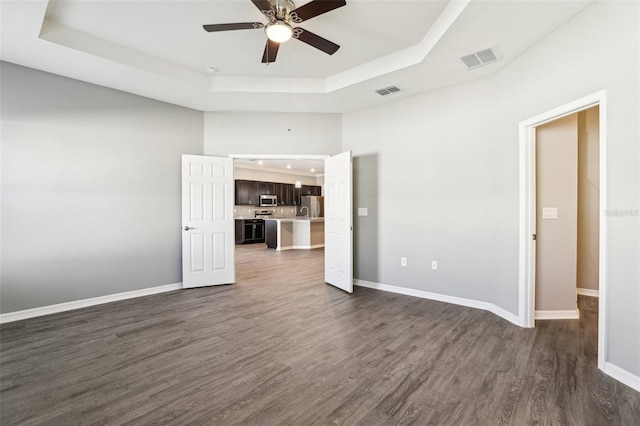 spare room with dark wood-type flooring, a raised ceiling, visible vents, and baseboards