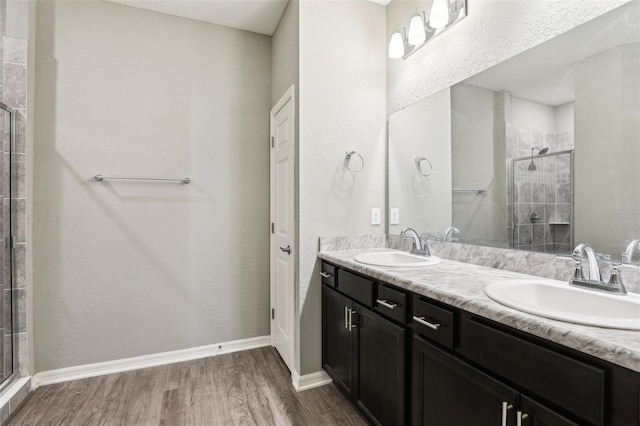 bathroom featuring double vanity, wood finished floors, a stall shower, and a sink