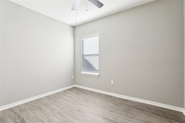 empty room with wood finished floors, a ceiling fan, and baseboards