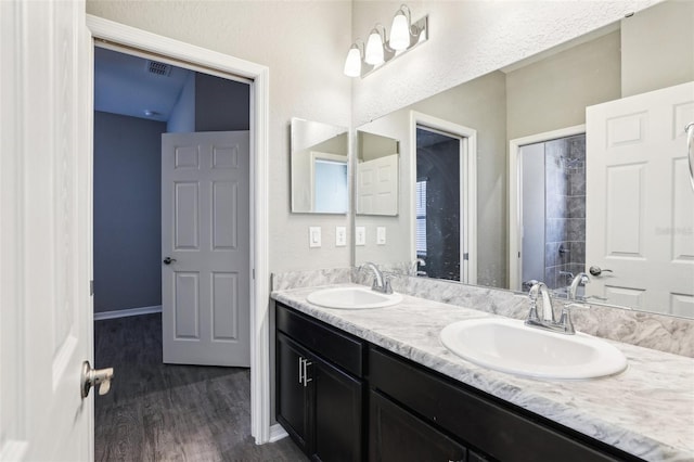 bathroom with double vanity, wood finished floors, a sink, and visible vents