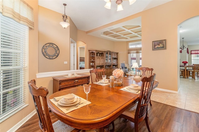 dining space featuring arched walkways, coffered ceiling, and wood finished floors