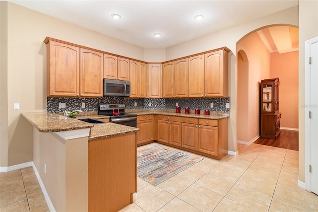 kitchen featuring a peninsula, light stone countertops, tasteful backsplash, and appliances with stainless steel finishes