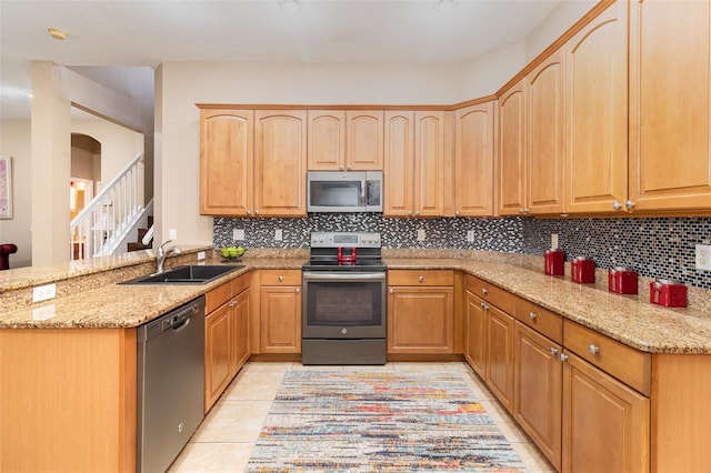 kitchen featuring light stone counters, stainless steel appliances, a peninsula, a sink, and backsplash