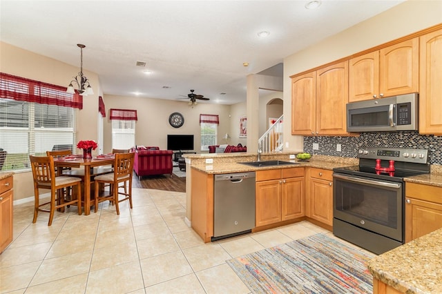 kitchen featuring light tile patterned flooring, stainless steel appliances, a peninsula, a sink, and backsplash