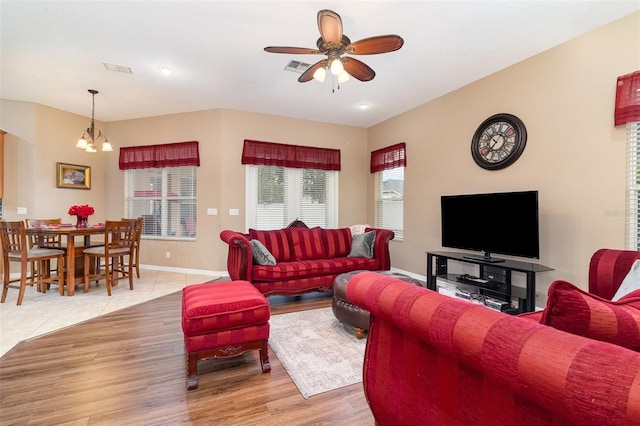 living area featuring light wood finished floors, visible vents, baseboards, and ceiling fan with notable chandelier