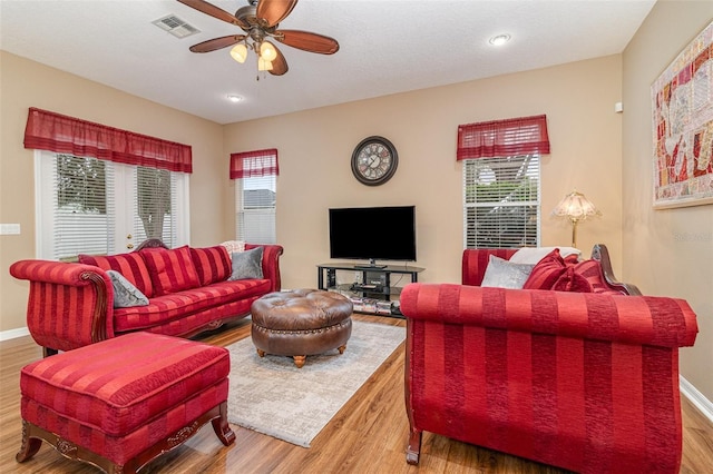 living room with baseboards, wood finished floors, visible vents, and a ceiling fan