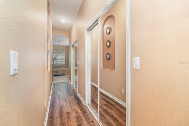 corridor featuring arched walkways, wood finished floors, and baseboards