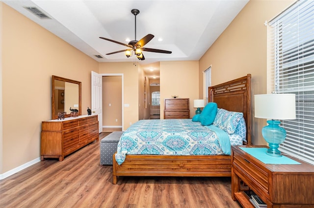 bedroom featuring a raised ceiling, visible vents, baseboards, and wood finished floors