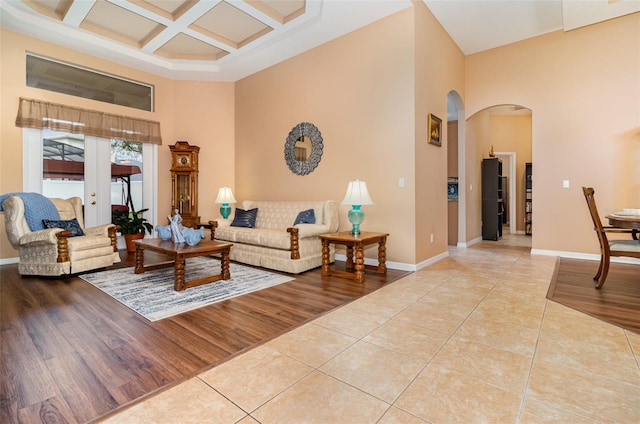 living area with arched walkways, light tile patterned flooring, coffered ceiling, and a towering ceiling