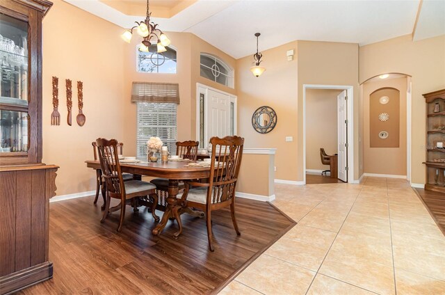 dining room with arched walkways, light wood finished floors, lofted ceiling, an inviting chandelier, and baseboards