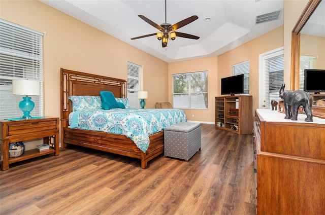 bedroom with baseboards, visible vents, ceiling fan, wood finished floors, and a tray ceiling