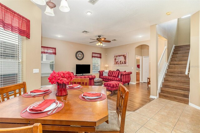 dining area with arched walkways, light tile patterned floors, a ceiling fan, visible vents, and stairway