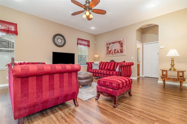 living area featuring baseboards, ceiling fan, arched walkways, and wood finished floors