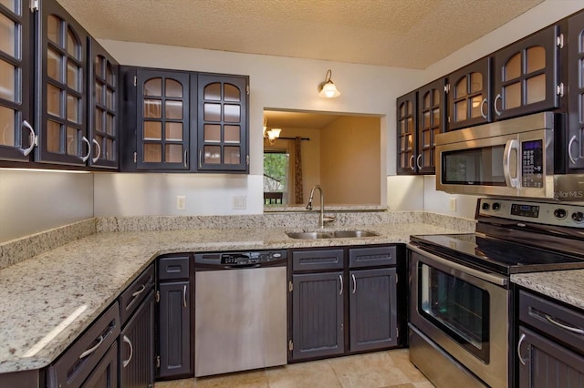 kitchen featuring a textured ceiling, glass insert cabinets, stainless steel appliances, and a sink