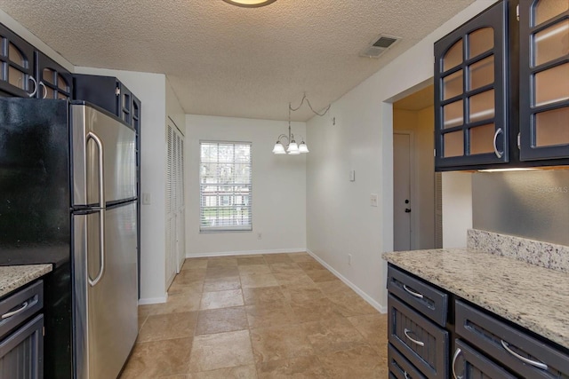 kitchen featuring wall oven, visible vents, glass insert cabinets, freestanding refrigerator, and a notable chandelier