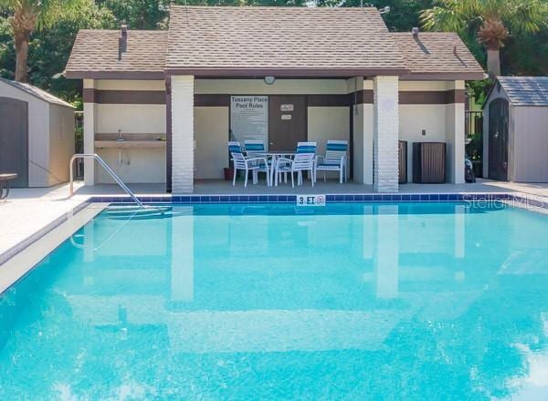 community pool with an outbuilding, a patio, a storage unit, and an exterior structure