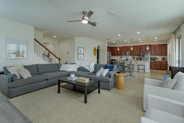 living area with arched walkways, light tile patterned floors, recessed lighting, stairway, and a ceiling fan