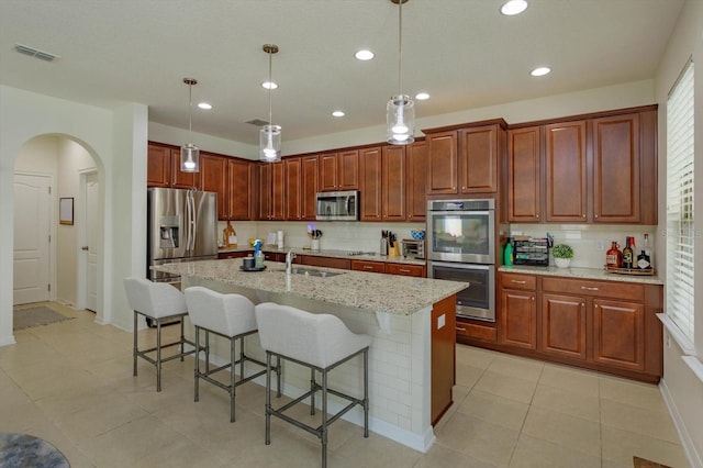 kitchen with a center island with sink, appliances with stainless steel finishes, pendant lighting, and a kitchen breakfast bar