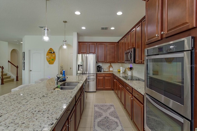 kitchen with arched walkways, decorative light fixtures, decorative backsplash, appliances with stainless steel finishes, and a sink