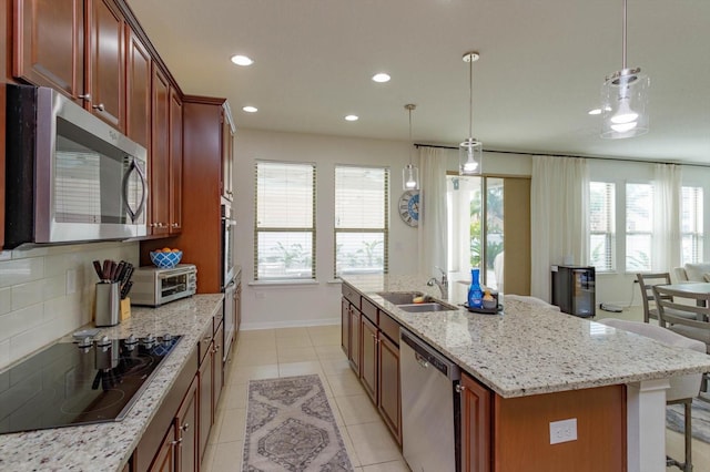 kitchen with stainless steel appliances, a sink, backsplash, an island with sink, and decorative light fixtures