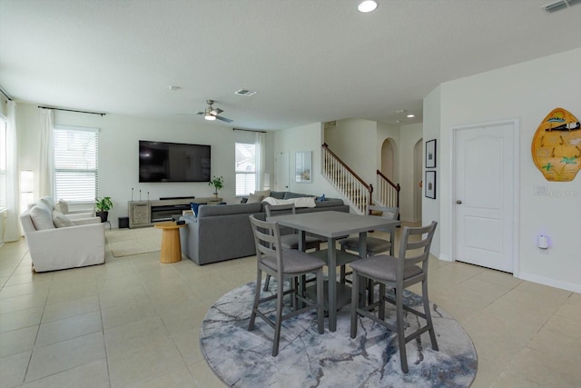 dining area with arched walkways, light tile patterned floors, visible vents, stairway, and ceiling fan