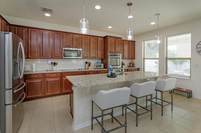 kitchen with appliances with stainless steel finishes, a center island with sink, hanging light fixtures, and a kitchen breakfast bar