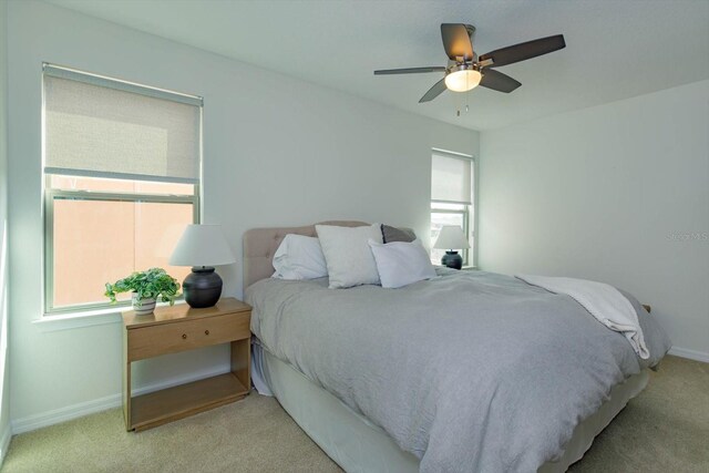 bedroom with light carpet, multiple windows, a ceiling fan, and baseboards