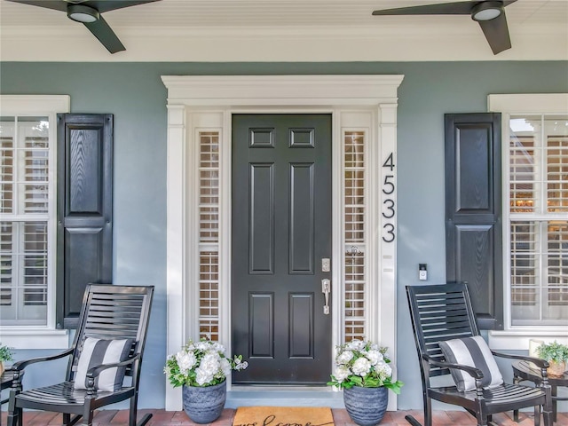 entrance to property featuring covered porch, ceiling fan, and stucco siding