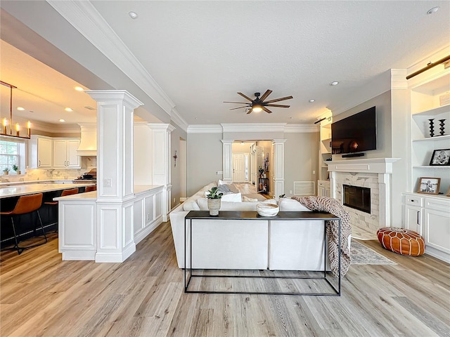 living area featuring decorative columns, a fireplace, ornamental molding, and light wood-style flooring