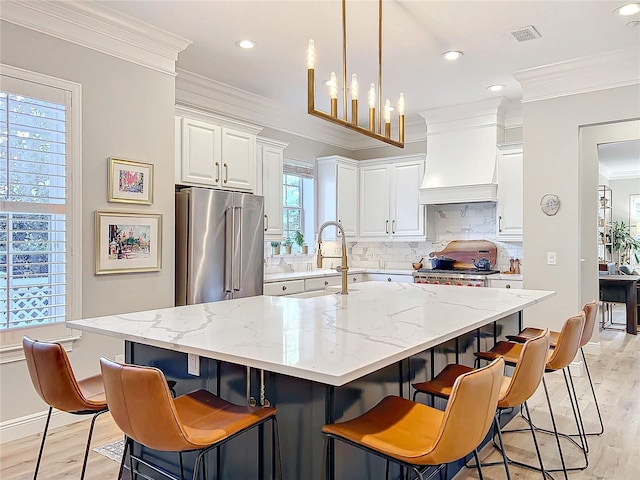 kitchen with custom range hood, visible vents, ornamental molding, light wood-style floors, and high quality fridge