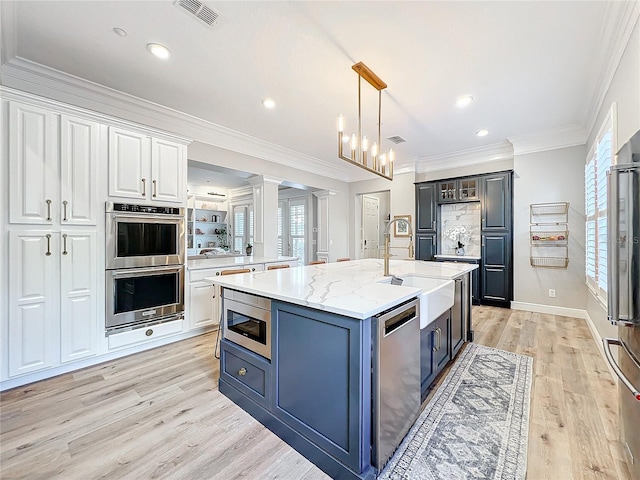 kitchen featuring a center island with sink, stainless steel appliances, visible vents, ornamental molding, and a sink