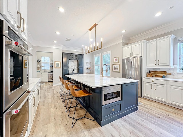 kitchen with light stone countertops, light wood finished floors, appliances with stainless steel finishes, and white cabinets