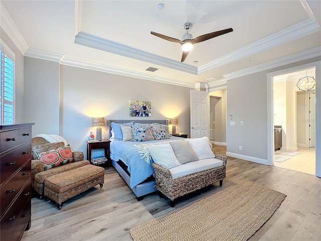 bedroom with a tray ceiling, baseboards, crown molding, and light wood finished floors