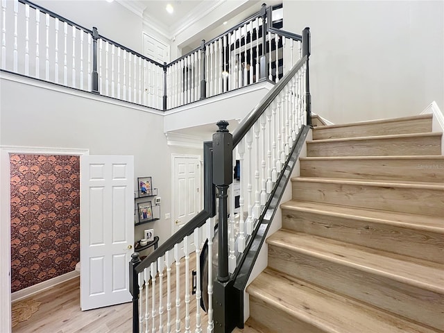 stairway with a towering ceiling, baseboards, ornamental molding, and wood finished floors