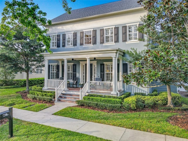 view of front of home featuring covered porch, a shingled roof, a ceiling fan, stucco siding, and a front lawn